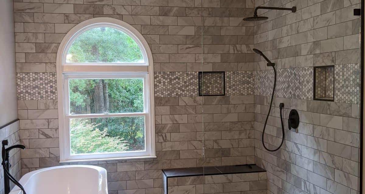 Bathroom with bathtub on the left wall and black shower head on the right, window is on the back marble like brick wall design , to the right of the window is a small seating ledge