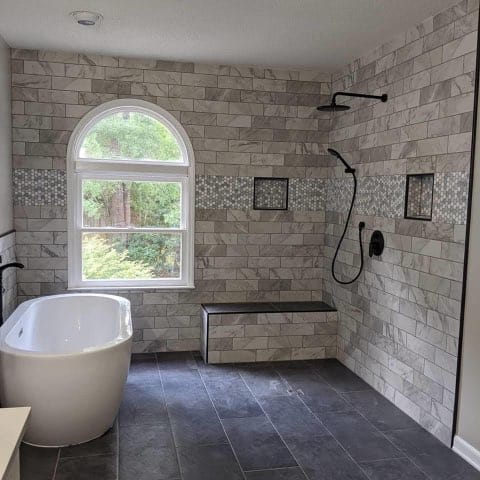 Bathroom with bathtub on the left wall and black shower head on the right, window is on the back marble like brick wall design , to the right of the window is a small seating ledge
